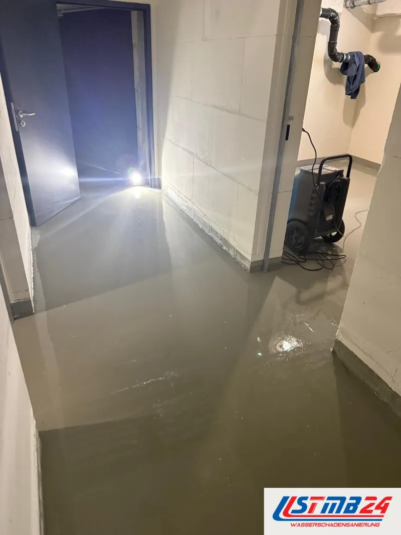 24-Stunden-Notdienst: Wasser steht im Kellergang bis an die Wände, rechts ein blauer Bautrockner, an der Wand Abwasserrohre