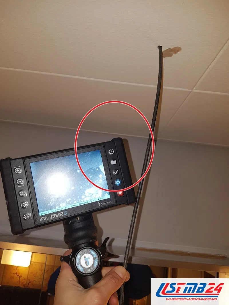 Endoskop mit Monitor, die Sonde führt durch eine kleine Bohrung in eine Decke aus Paneelen, ein roter Kreis markiert die Stelle