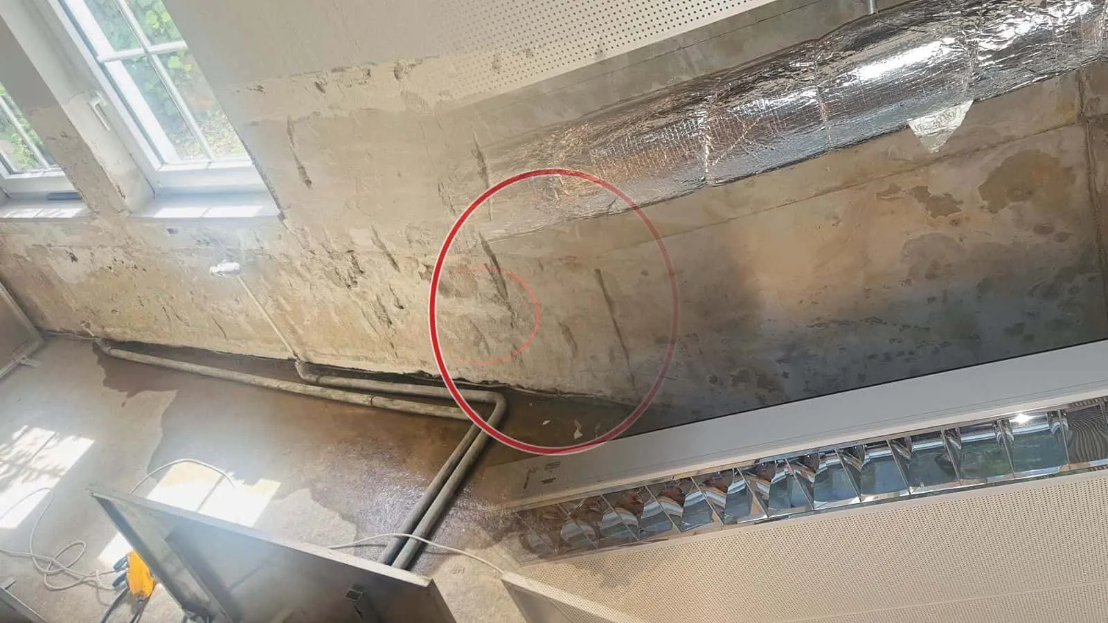 Geöffnete Rasterdecke mit Lüftungsrohr in Silberfolie und nasser Rohdecke über einer Rasterleuchte