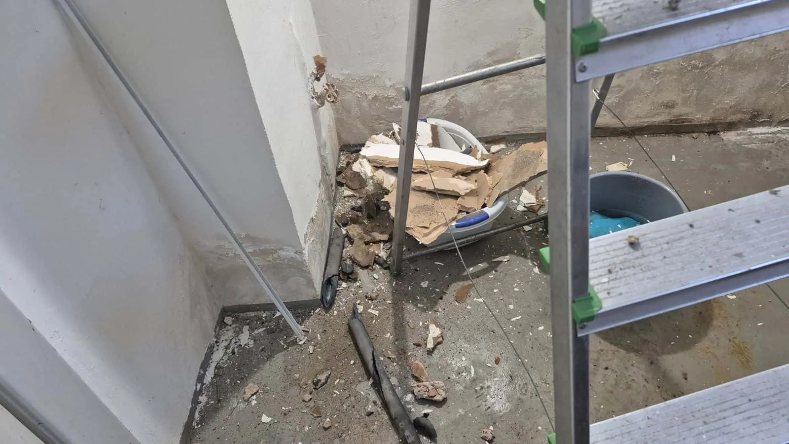 Weiße Wandecke im Rückbau, davor Schutt, Rohrstücke und eine Leiter