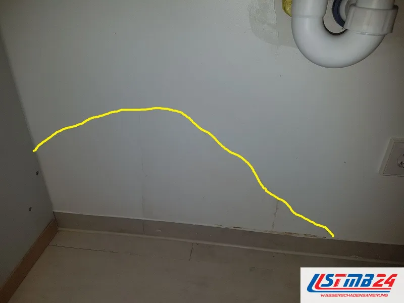 Helle Wand unter einem weißen Abflussbogen, eine gelbe Linie umfährt die feuchte Fläche bis zur Sockelleiste