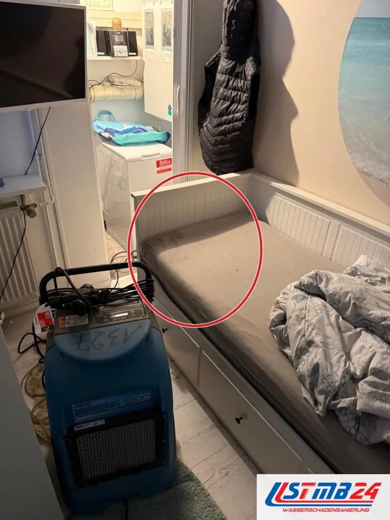 Blauer Kondenstrockner neben einem Bett in einem bewohnten Kinderzimmer, ein roter Kreis markiert die Stelle