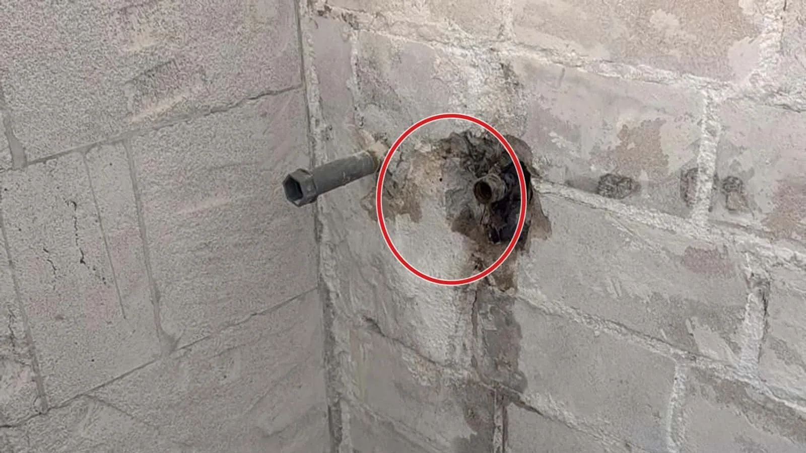 Rohrstutzen in einer weißen Ziegelwand im Keller, darunter die dunkle Wasserspur zum Bodenablauf, ein roter Kreis markiert den Stutzen