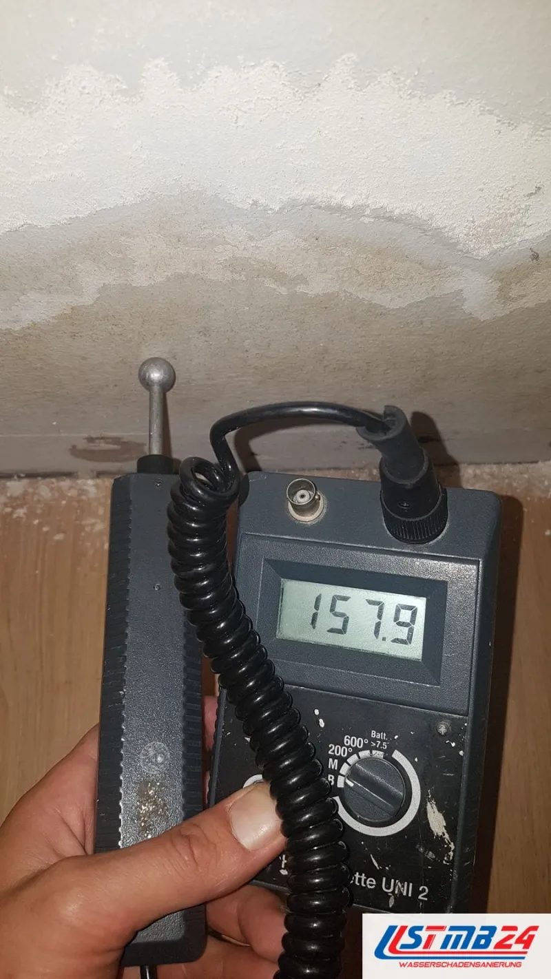Feuchtemessgerät mit 157,9 auf dem Display unter einer Decke mit hellen Wasserrändern im Putz