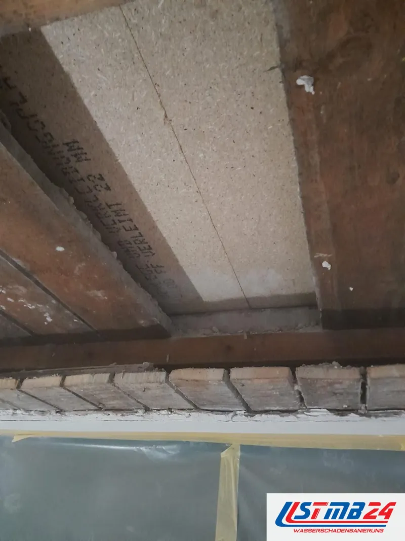 Geöffnete Decke: dunkle alte Holzbalken liegen auf dem Mauerwerk auf, dazwischen helle Spanplatten, darunter eine Schutzfolie