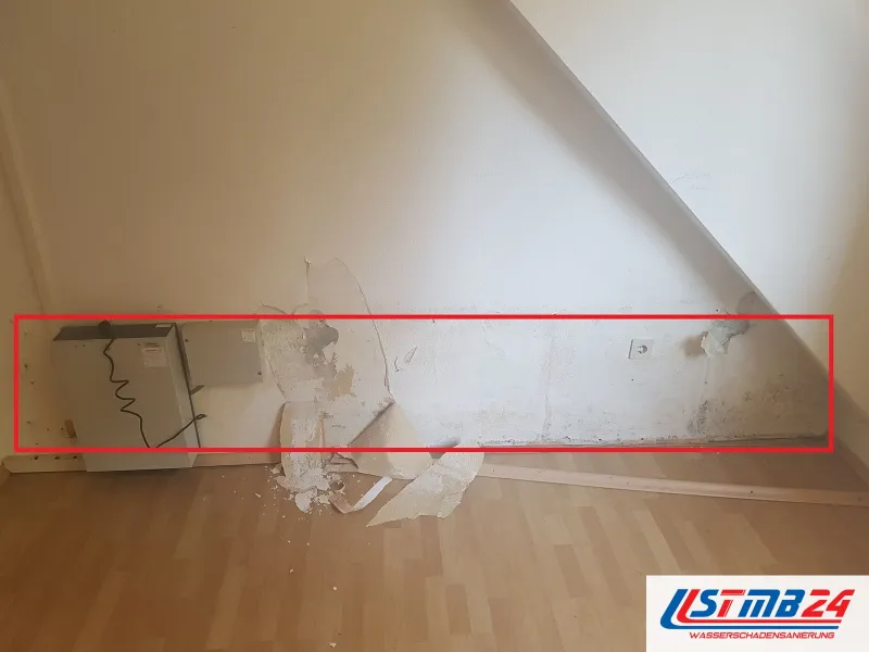 Zimmer unter der Dachschräge, abgelöste Tapete am Boden, ein rotes Rechteck um den fleckigen Wandstreifen, links ein Gerät mit Kabel