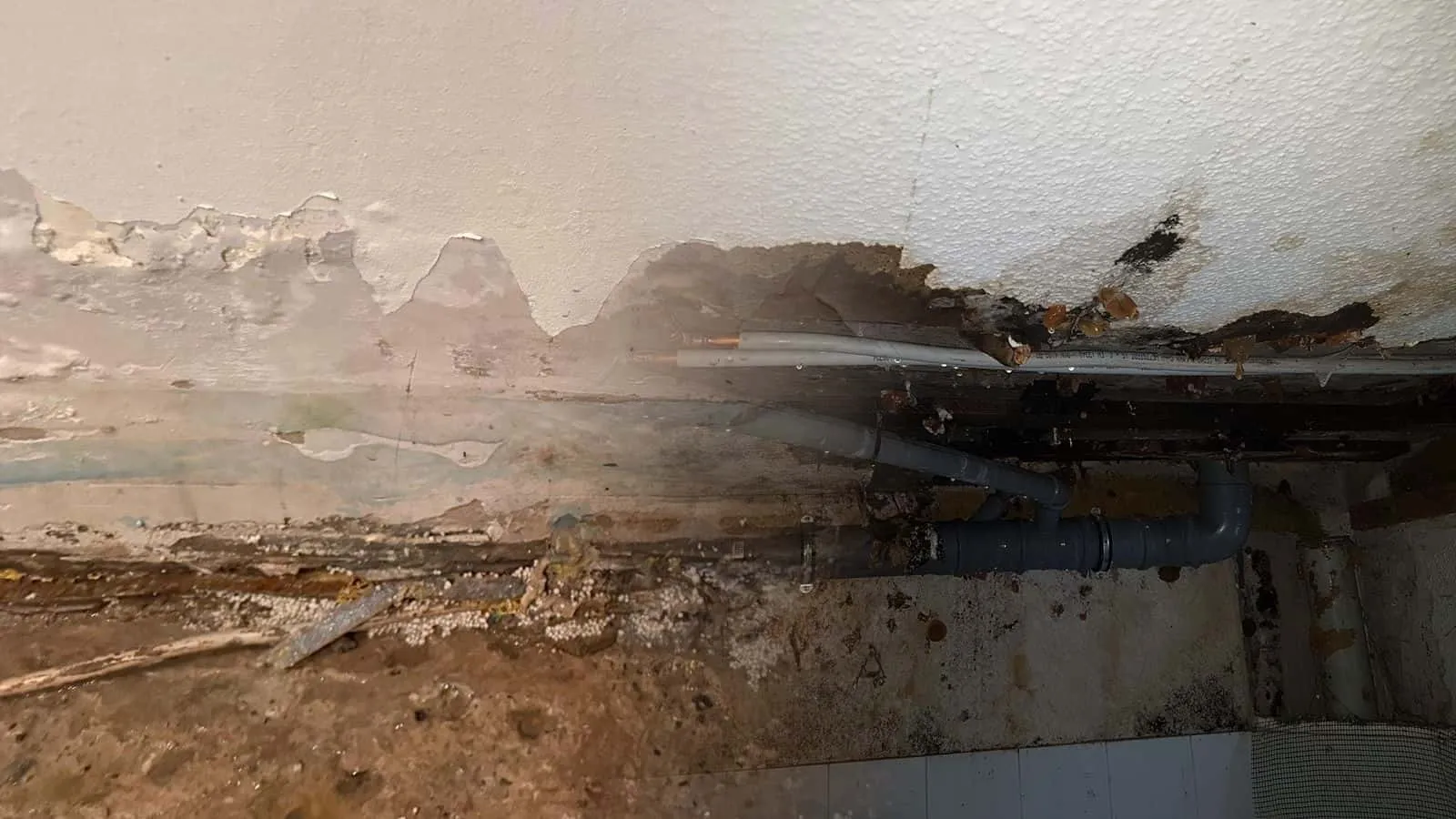Offene Decke mit Abwasserrohren und Leitungen, ringsum nasser Putz