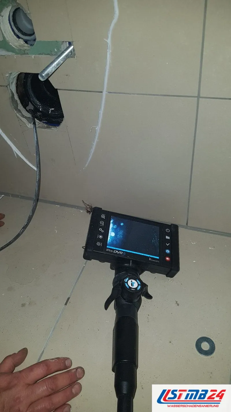 Kamera mit Monitor auf dem Fliesenboden, das Kabel führt in den geöffneten Abfluss an der Wand