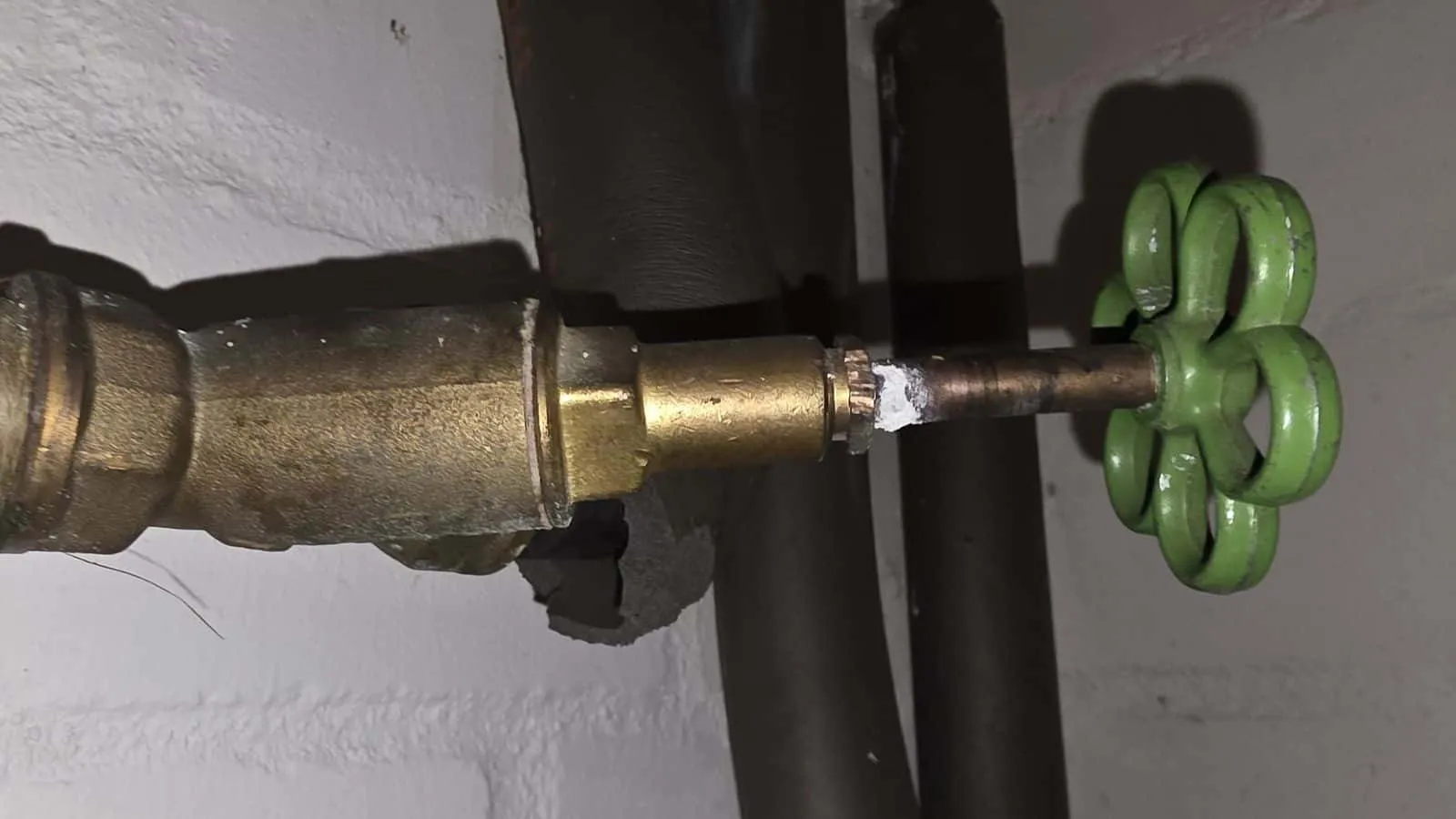 Messingventil mit grünem Handrad an einer hell gestrichenen Kellerwand