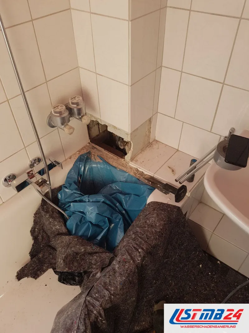 Geöffnete Fliesenwand neben zwei Wasserzählern im Bad, die Badewanne mit Folie und Malervlies abgedeckt