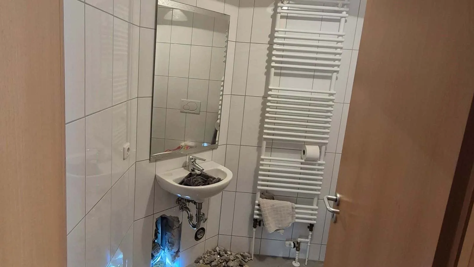 Blick durch die Tür in ein Bad mit Waschbecken, Spiegel und Handtuchheizkörper
