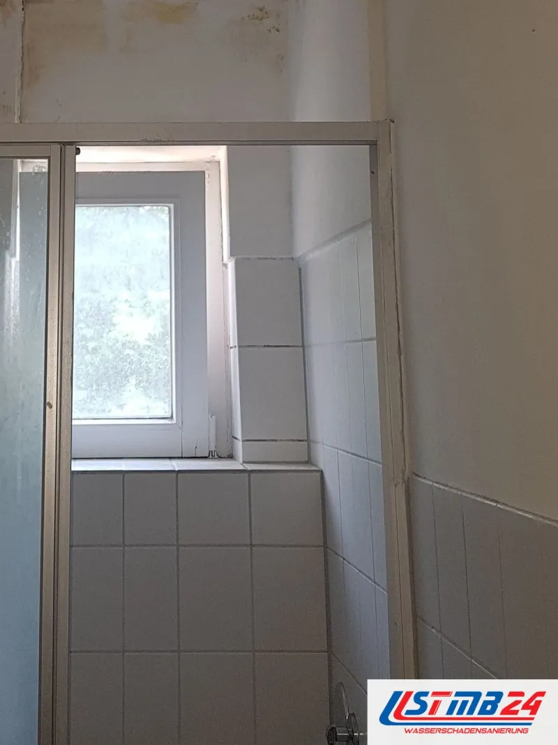 Schmales Bad mit Duschkabine und Fenster, oben an der Decke gelbbraune Wasserflecken
