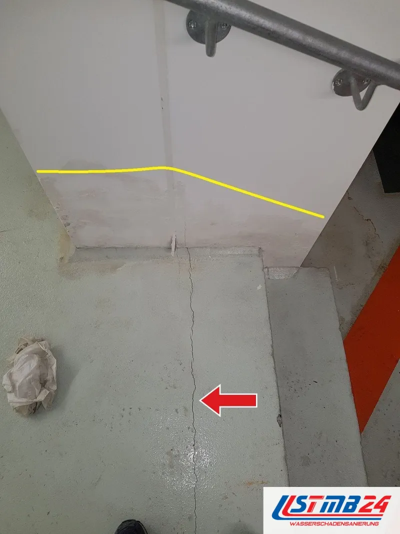 Treppenabsatz mit Handlauf, ein roter Pfeil zeigt auf den Riss im Estrich, eine gelbe Linie an der Wand markiert die Feuchtegrenze