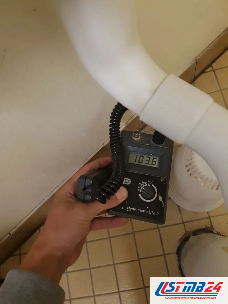 Messgerät mit Anzeige 103,6 unter einem weißen Abflussrohr über hellen Fliesen
