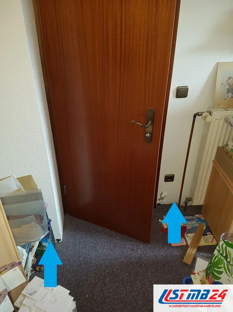 Flur vor einer Holztür, zwei blaue Pfeile zeigen auf den Boden