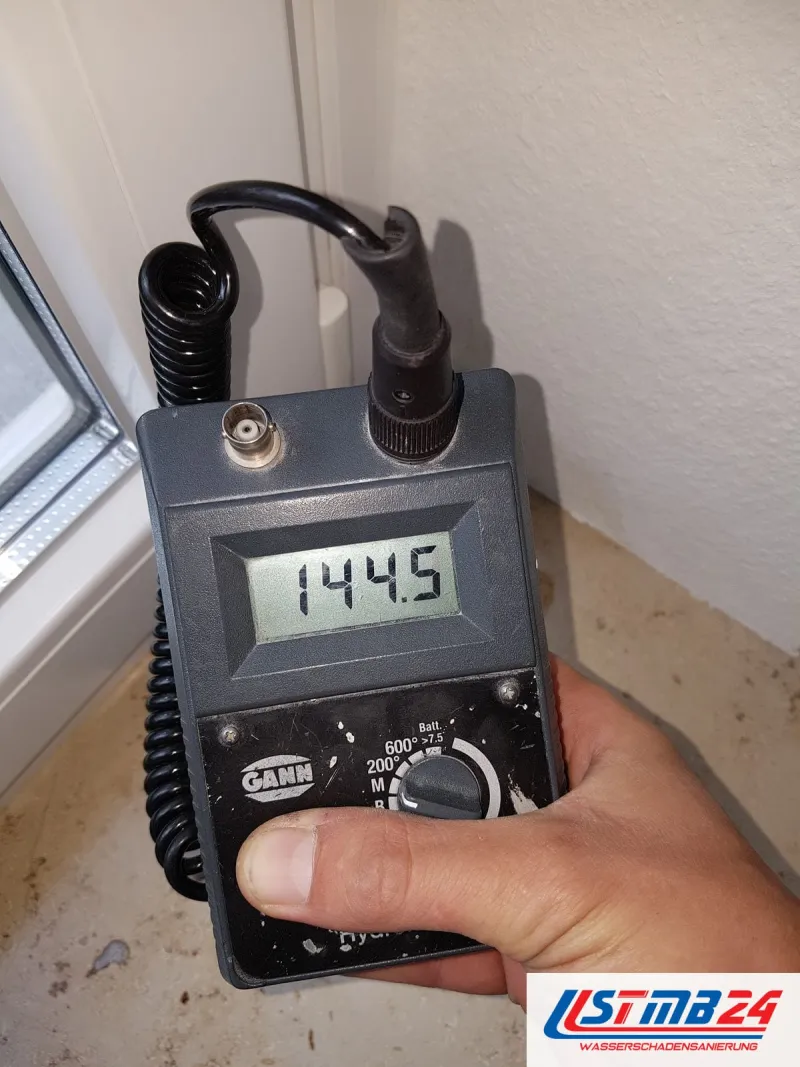 Feuchtemessgerät mit Anzeige 144,5 in einer Zimmerecke neben einem Fensterrahmen, am Boden Reste eines entfernten Belags