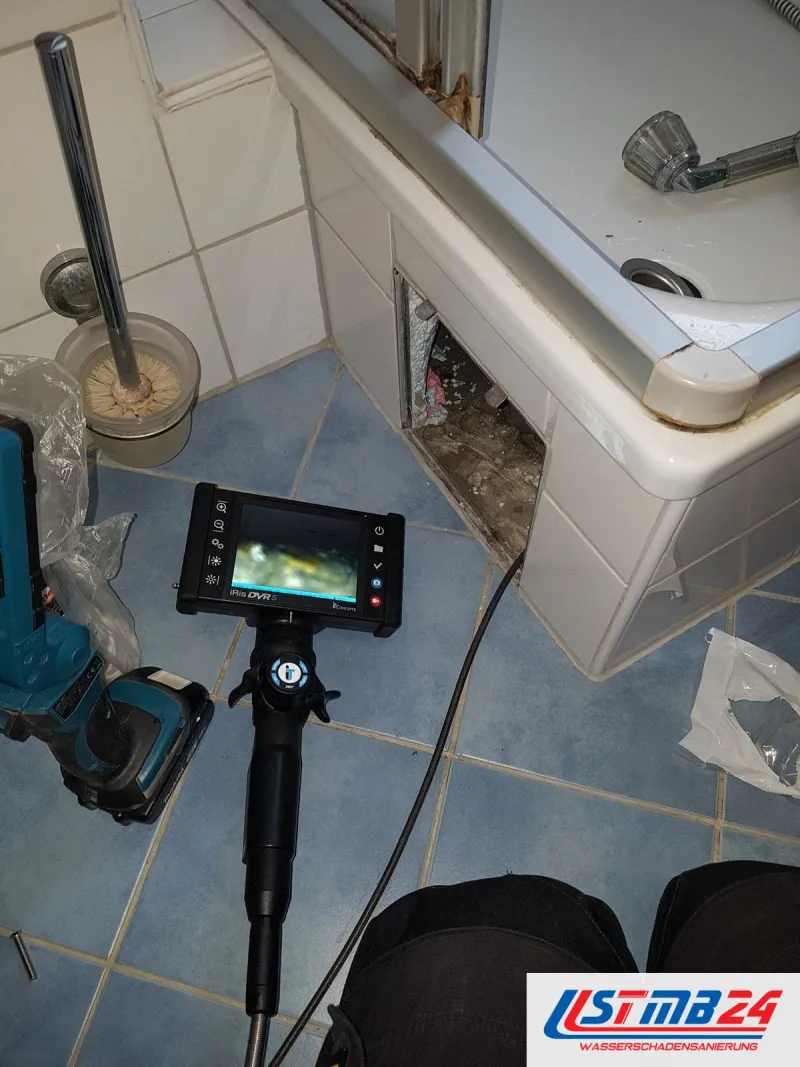 Endoskop mit Bildschirm auf blauen Bodenfliesen, die Schürze der Badewanne ist geöffnet, daneben ein Akkuschrauber