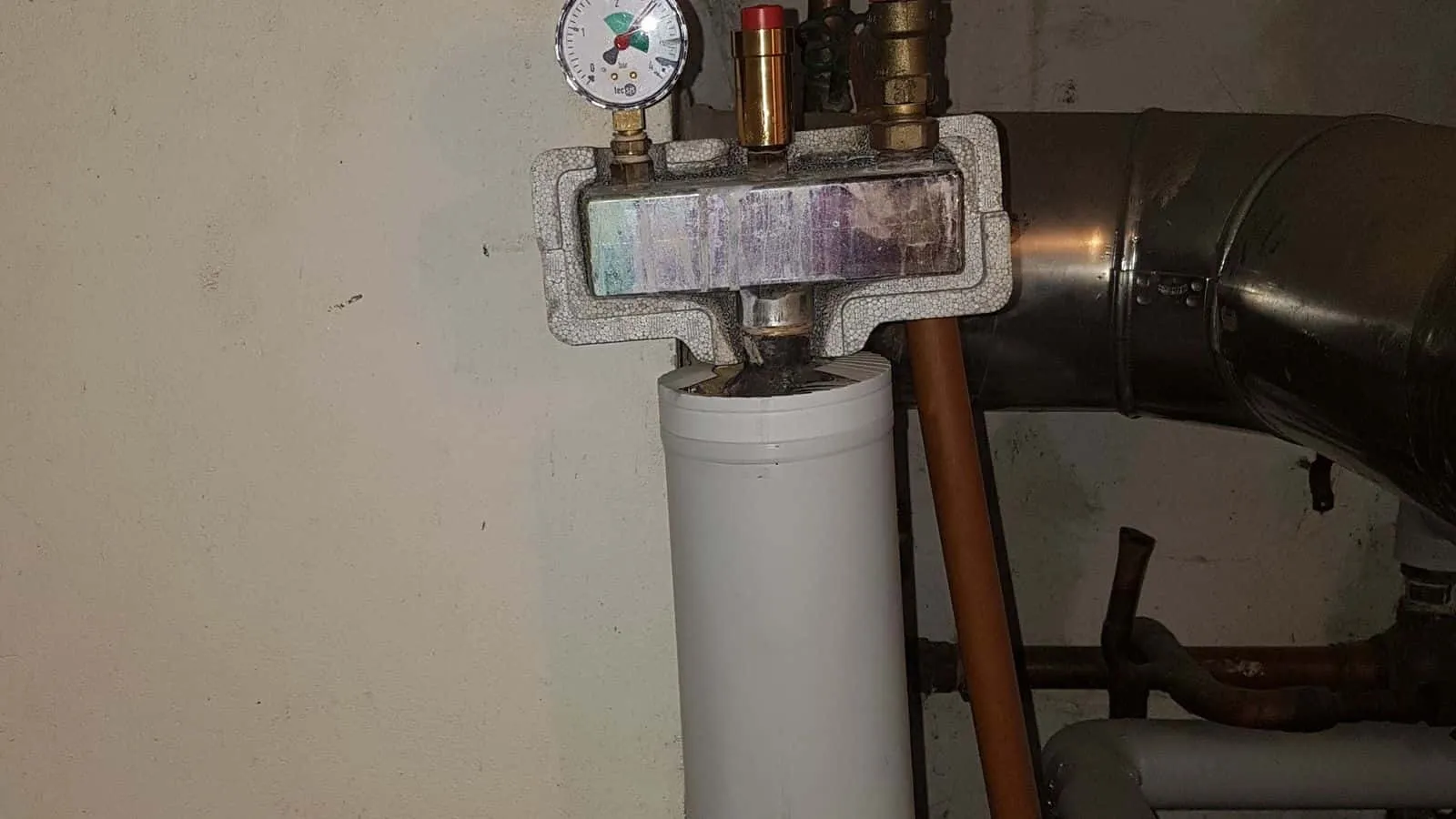Heizungsverteiler mit Manometer und roten Ventilen an einer hellen Kellerwand