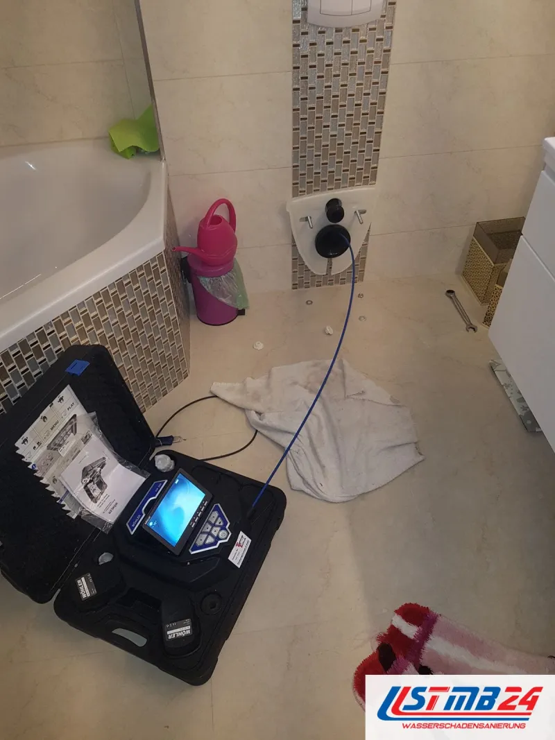 Bad mit Eckwanne und Mosaikstreifen, auf dem Boden ein geöffneter Kamerakoffer mit Monitor und ein Tuch