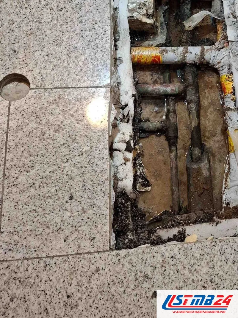 Ausgeschnittenes Feld in einem Granitboden, darunter Kupferleitungen mit Dämmung und eine nasse, dunkle Schüttung