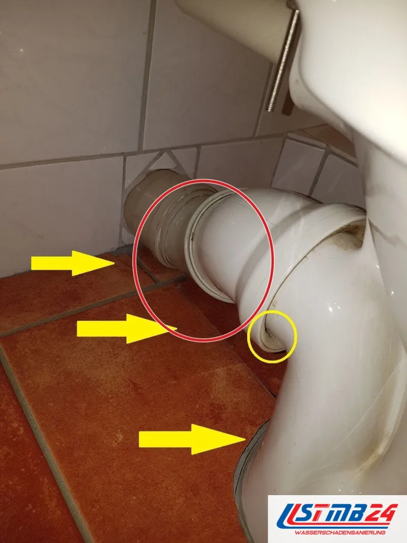 WC-Anschluss auf rotbraunen Fliesen, gelbe Pfeile auf die Fuge, ein roter Kreis markiert die Stelle