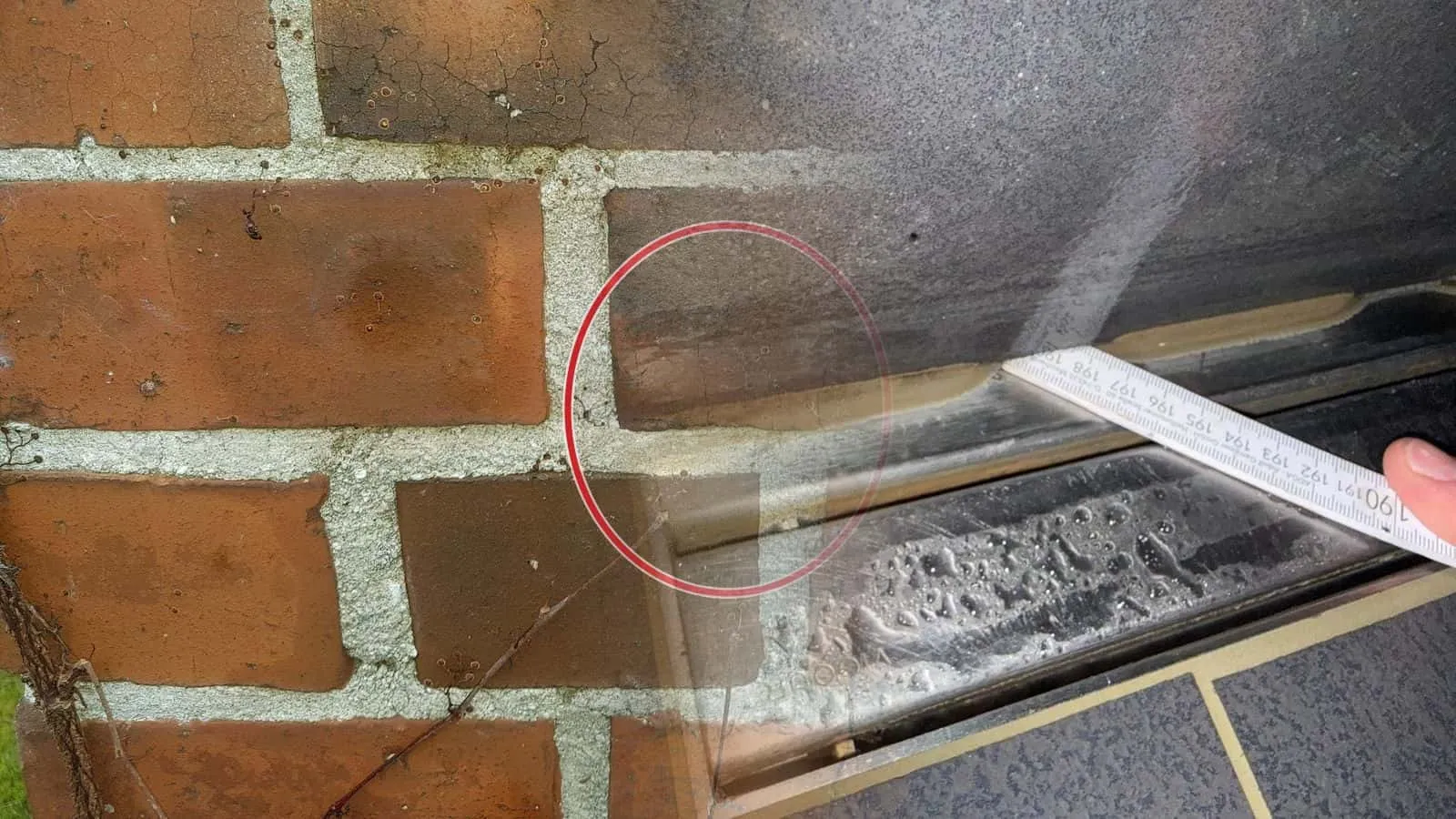 Duschrinne aus Edelstahl von oben, ein Zollstock liegt an der Fuge zur Wand, Tropfen auf dem Belag