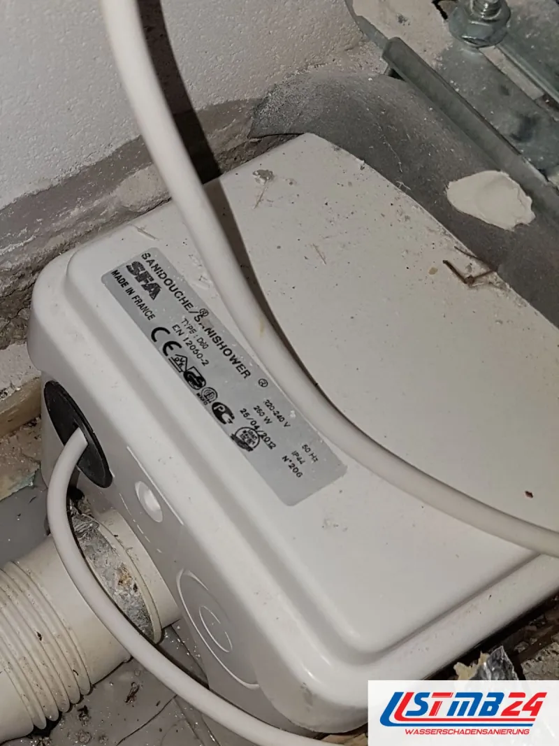 Kleine Hebeanlage in einer Bodenöffnung, ringsum freigelegte Abwasserrohre und Dämmung