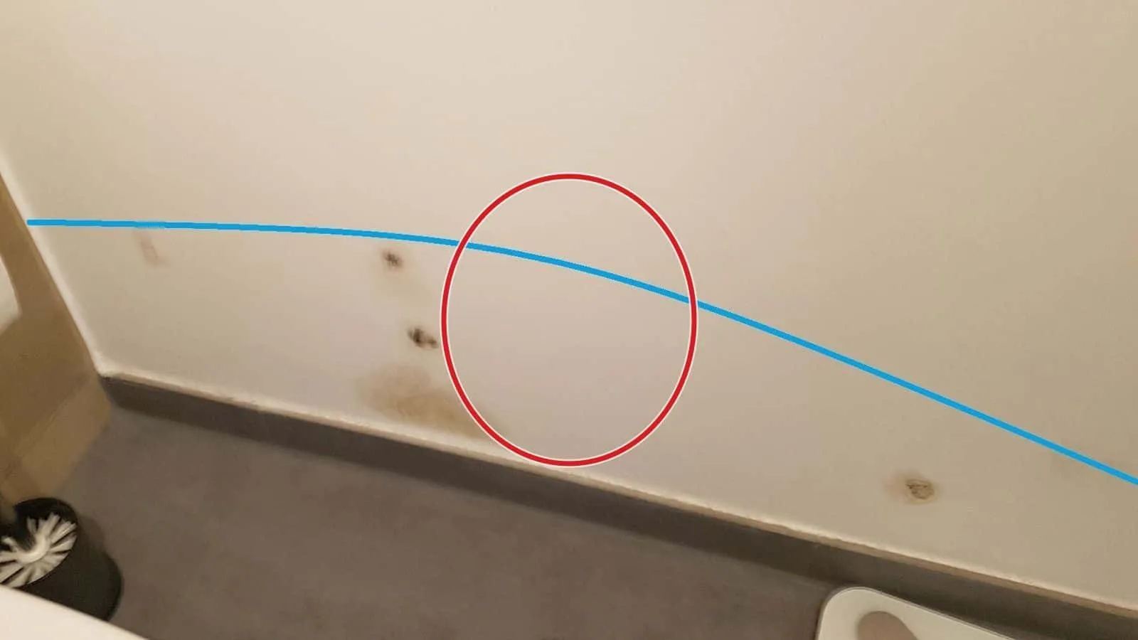 Blaue Linie über braunen Wasserflecken an der WC-Wand, darüber die Markierung der Feuchtegrenze