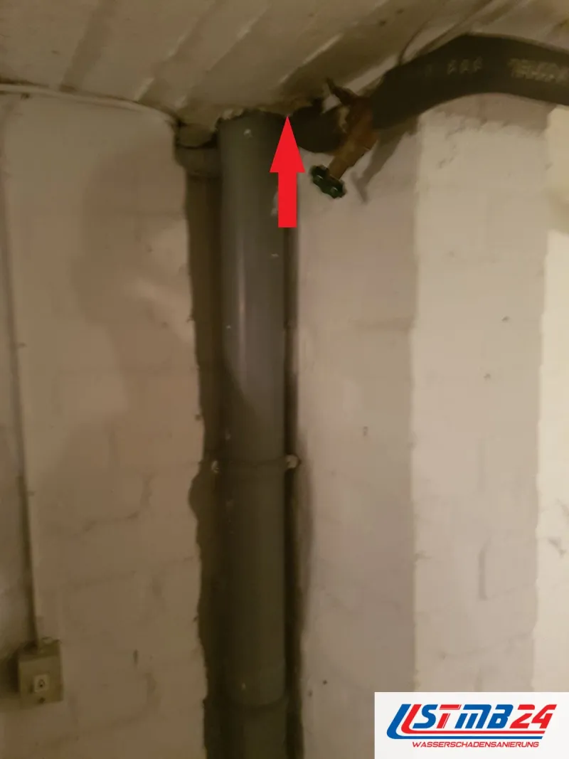 Graues Fallrohr im Keller, ein roter Pfeil zeigt auf den Anschluss unter der Decke