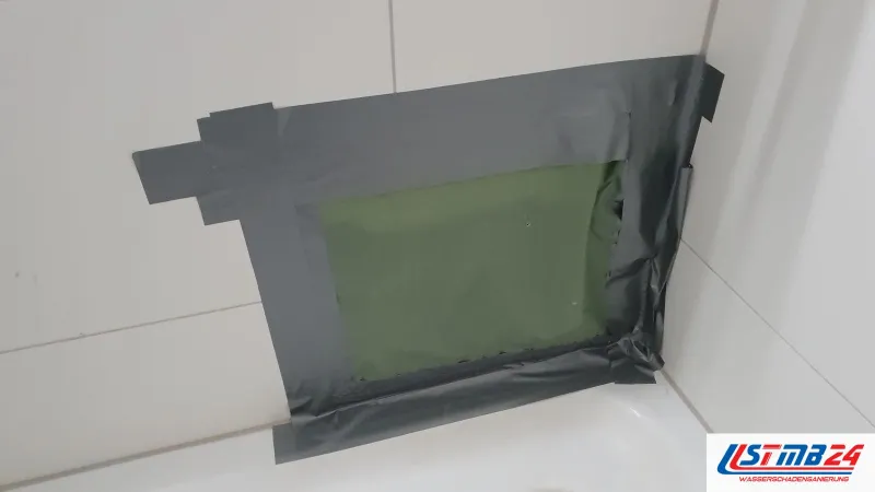 Öffnung in der Fliesenwand über der Badewanne, mit grüner Folie und grauem Klebeband vorläufig verschlossen