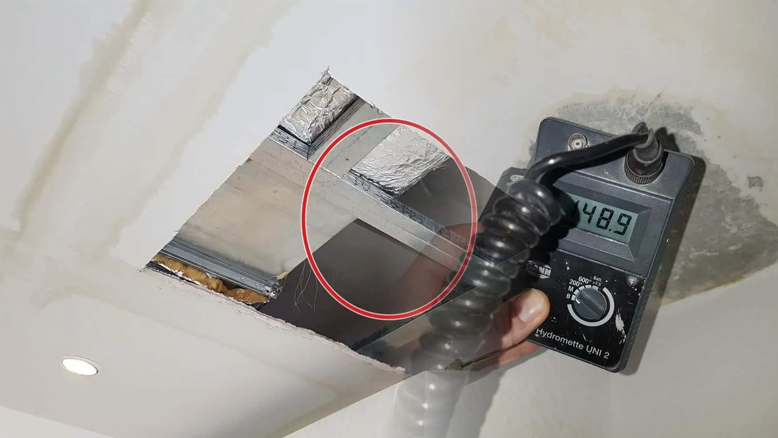 Feuchtemessgerät mit Anzeige 148,9 in einem grau verfärbten Fleck an der Decke, ringsum gelbliche Wasserränder