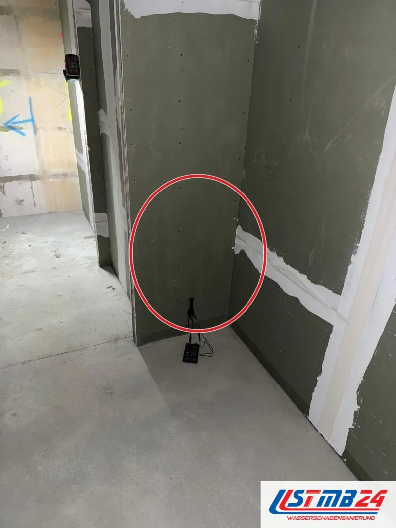 Nische aus grünen Gipsplatten im Neubau, gespachtelte Stöße, am Boden ein Gerät mit Kabel, ein roter Kreis markiert die Stelle