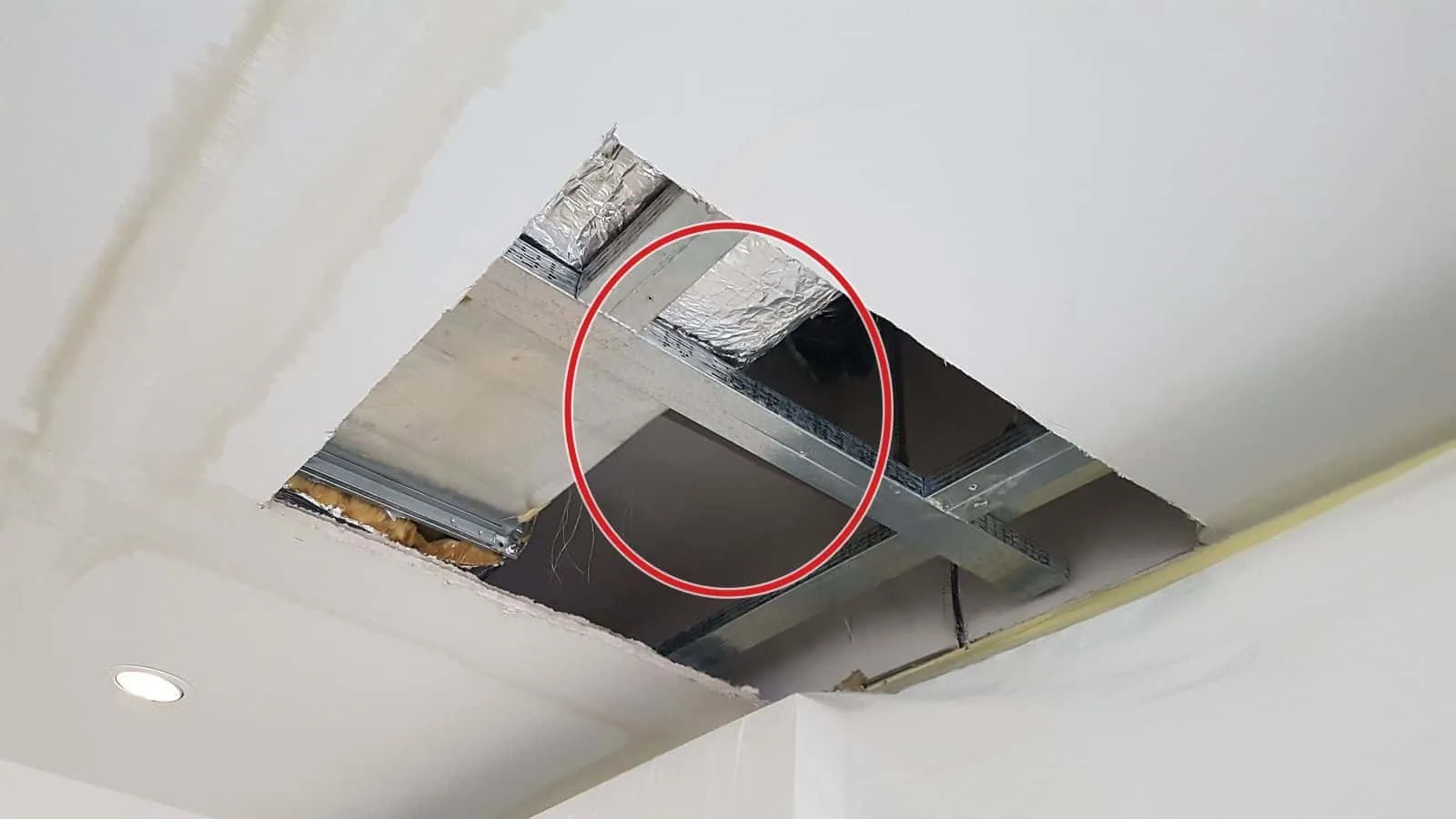 Ausgeschnittene Öffnung in einer Gipskartondecke, darüber Metallprofile, Alu-Dämmung und eine Leitung