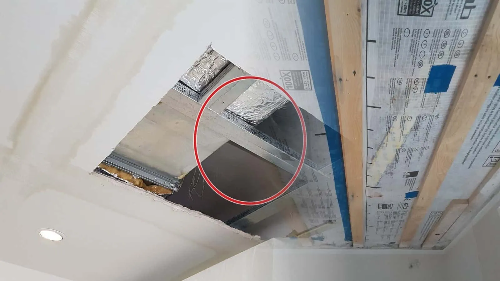 Dampfbremse zwischen der Holzlattung einer Decke, dunkle Feuchteflecken auf der Folie, blaues Klebeband an den Stößen