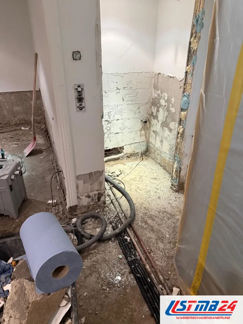 Raum mit abgeschlagenem Wandputz, am Boden laufen Schläuche der Trocknung an der Wand entlang, rechts eine Staubschutzwand