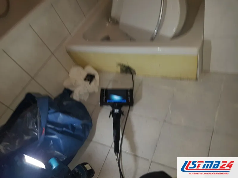 Endoskop mit Monitor auf dem Fliesenboden vor einer Wanne, daneben eine blaue Tasche und eine Lampe