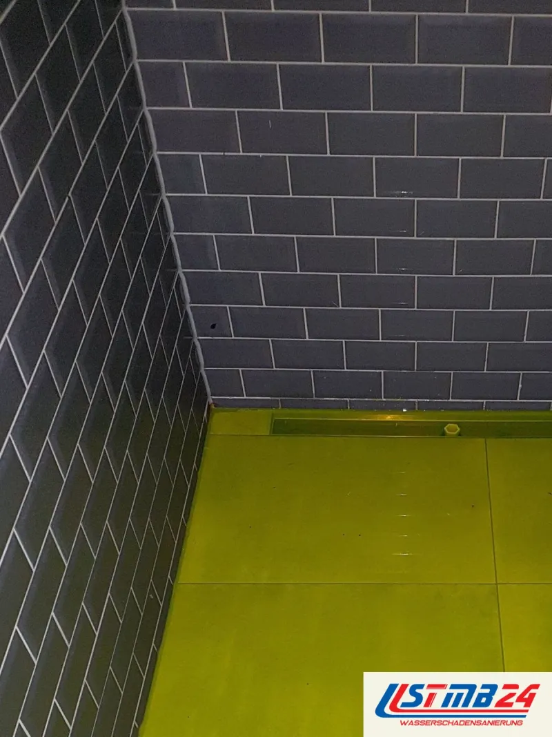 Bodengleiche Dusche mit grauen Metrofliesen an der Wand, der Boden steht unter gelb eingefärbtem Wasser