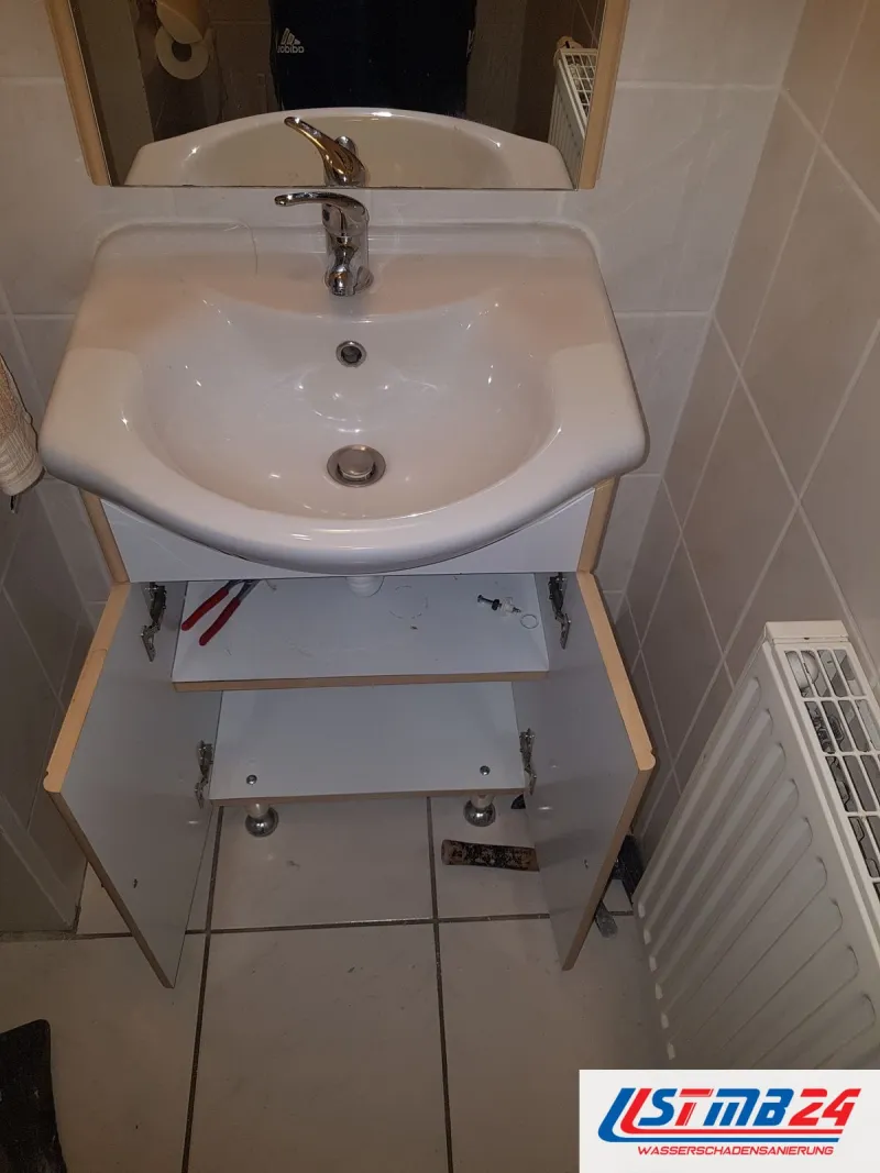 Waschtisch mit offenem Unterschrank neben einem Heizkörper, die Anschlüsse unter dem Becken liegen frei