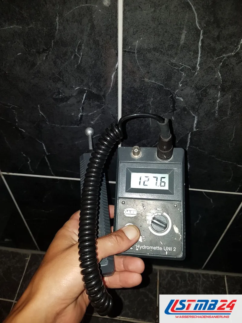 Feuchtemessgerät mit Anzeige 127,6 vor dunklen Wandfliesen mit heller Marmorzeichnung