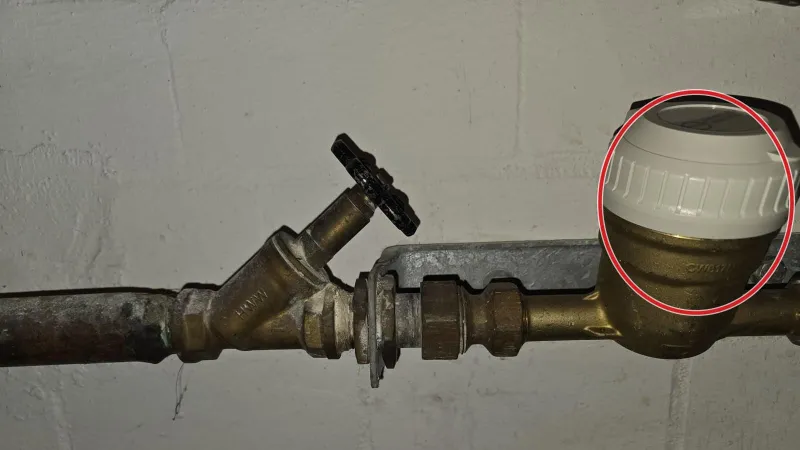 Hausanschluss im Keller: Messingventil mit Entleerung vor dem Wasserz&auml;hler mit wei&szlig;er Kappe, ein roter Kreis markiert den Z&auml;hler