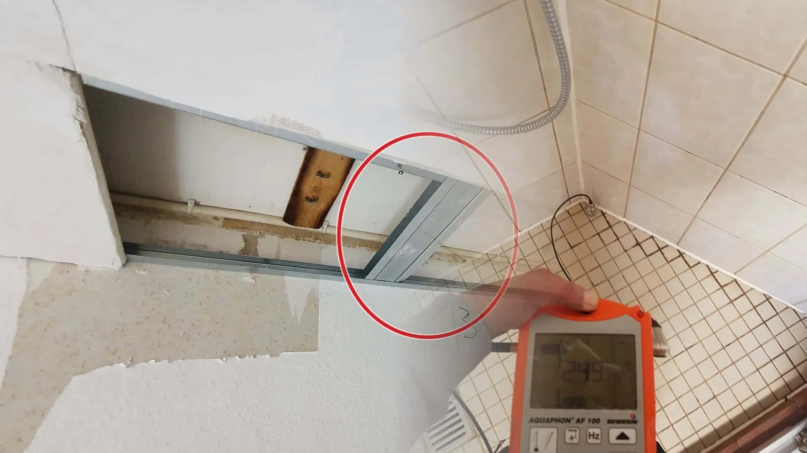 Horchgerät der elektroakustischen Ortung in der Hand, das Mikrofon steht in der Duschecke auf dem Mosaikboden