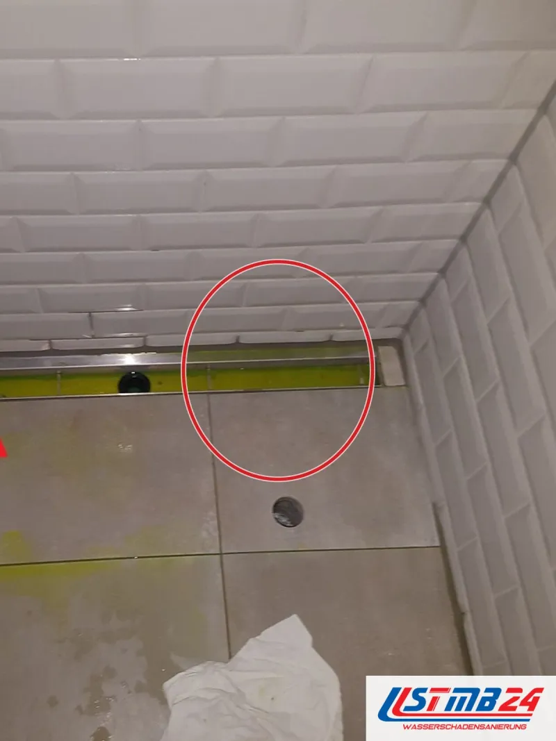 Bodengleiche Dusche mit weißen Wandfliesen, gelbes Färbemittel in der Duschrinne, rote Pfeile auf die Ränder, roter Kreis an der Stelle