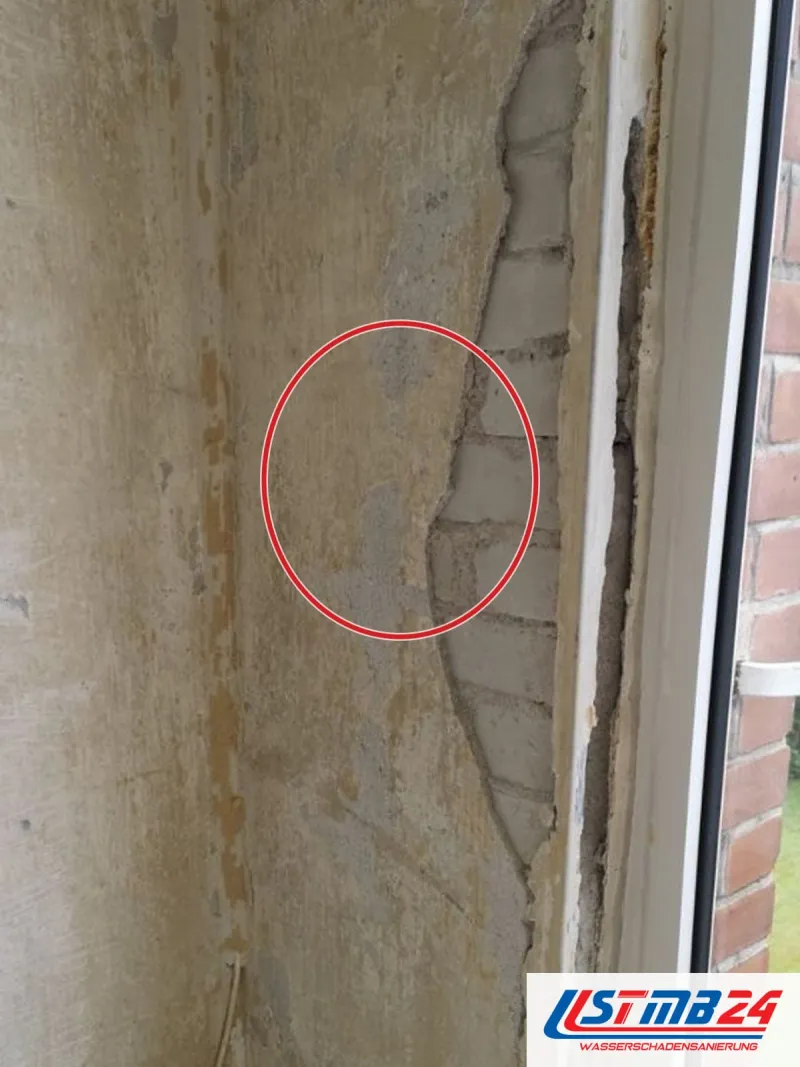 Fensterlaibung mit abgelöstem Putz bis aufs Mauerwerk, die Wand fleckig, unten Schimmel, ein roter Kreis markiert die Stelle