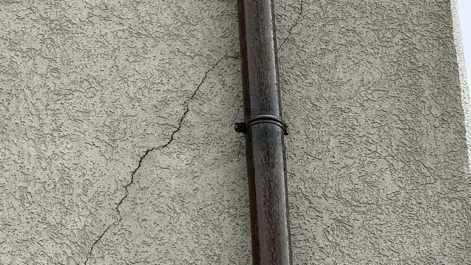 Putzfassade mit Fallrohr und einem Riss im Putz