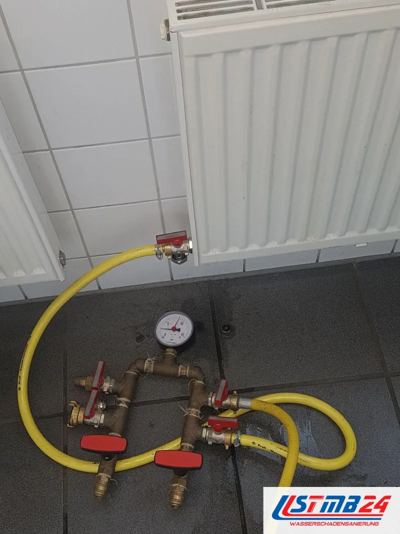 Druckprüfgerät mit gelben Schläuchen vor zwei Heizkörpern