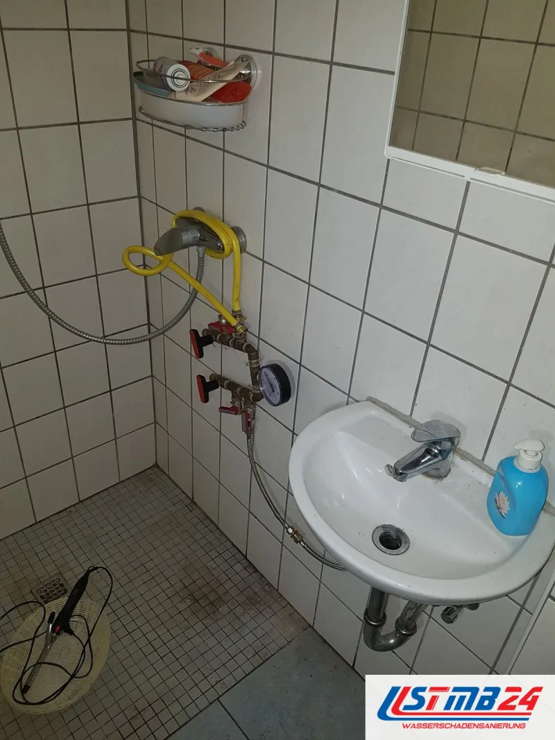 Kleines Bad mit Waschbecken, ein Prüfgerät hängt am Wandanschluss