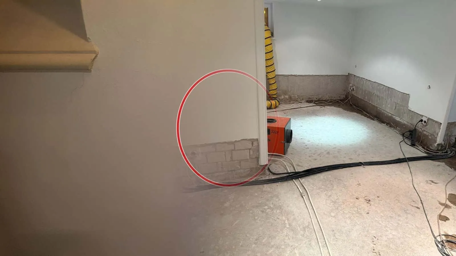 Souterrain mit abgeschlagenem Sockelputz, ein orangefarbenes Trocknungsgerät auf dem Estrich, Kabel am Boden