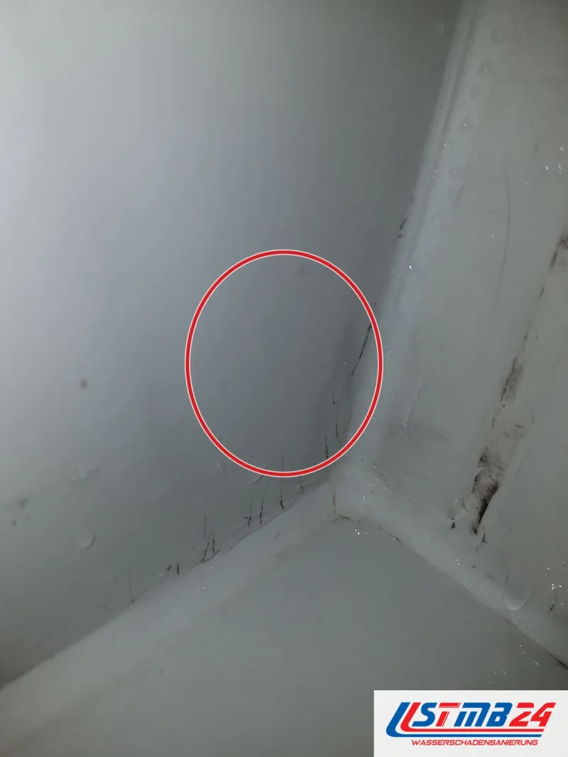 Ecke einer Duschtasse, in der Silikonfuge zur Wand schwarze Stellen und ein Riss, ein roter Kreis markiert die Stelle