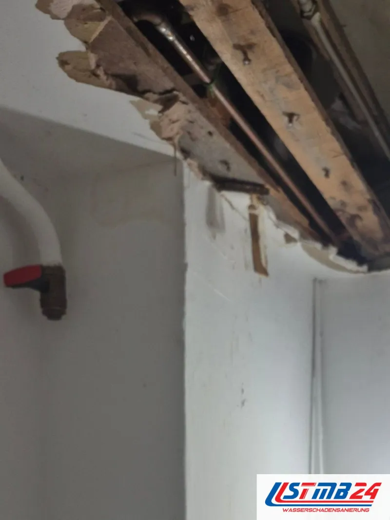 Geöffnete Decke über einem schmalen Raum, alte Holzteile hängen heraus, unten ein weißes Rohr mit rotem Ventil