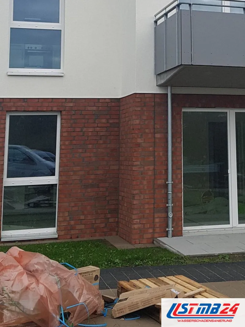 Neubau mit Balkon über der Terrassentür, unten Klinker, oben heller Putz, davor Paletten und ein orangefarbener Sack